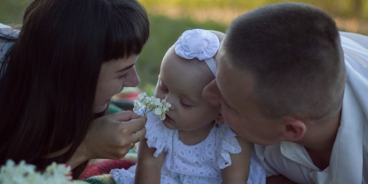 A loving family moment with parents and baby at a sunny outdoor picnic.