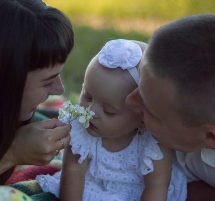 A loving family moment with parents and baby at a sunny outdoor picnic.
