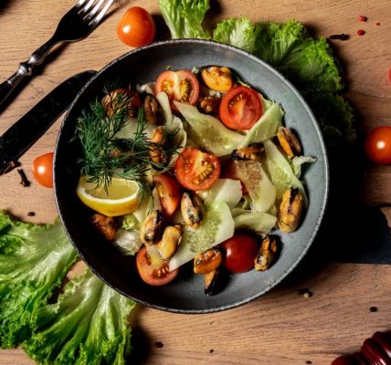A vibrant salad featuring cherry tomatoes, mussels, and fresh lettuce with a lemon garnish. Perfect for a healthy meal.