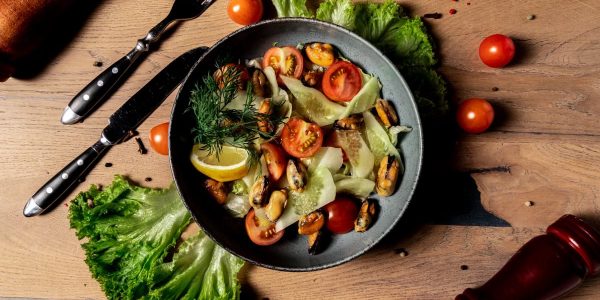 A vibrant salad featuring cherry tomatoes, mussels, and fresh lettuce with a lemon garnish. Perfect for a healthy meal.